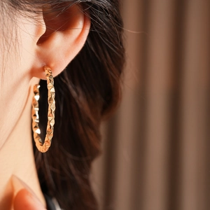 Detail shot of gold geometric C-shaped earrings with diamond-cut texture on a model