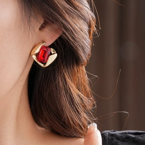 Close-up of a red square gemstone earring set in a gold geometric base on a model