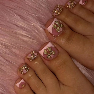 Pink press-on toe nails with golden bows and rhinestone floral designs on plush fabric