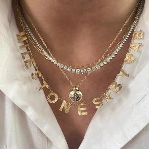 Vue détaillée de colliers dorés superposés avec pendentif coccinelle et breloques lettres