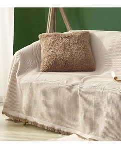 Close-up of beige waffle texture sofa cover with fringe details and a brown plush pillow