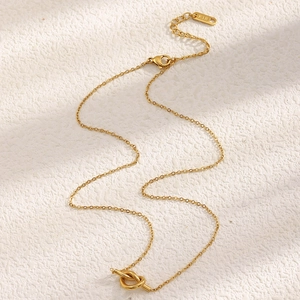 Detailed view of an 18K gold-plated knotted pendant on a textured cream surface