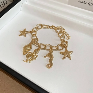 Detail of gold ocean charm bracelet with starfish and shell pendants in a white jewelry box