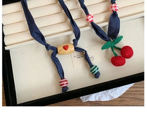 Detail of handmade crochet cherry charms and denim fabric straps on a long necklace