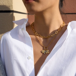 Detail of layered gold 18K clover and coin pendant necklace with sunlit texture