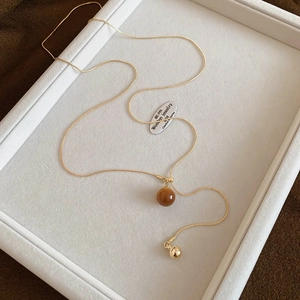 Detail of a golden snake chain necklace with an amber-colored tiger eye heart bead