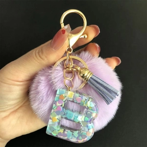 Porte-clés pompon violet avec lettre B en résine à paillettes et pompon bleu sur fond noir