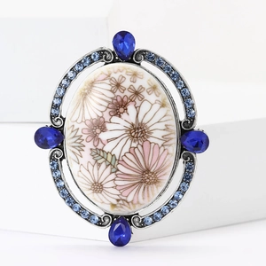 Detail of baroque brooch with floral enamel center and blue crystals in silver frame