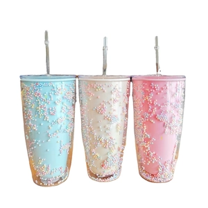 Three transparent double-wall tumblers with colorful foam beads and straws on white background