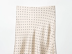 Détail d'une jupe en satin champagne avec motif à pois noirs et texture soyeuse