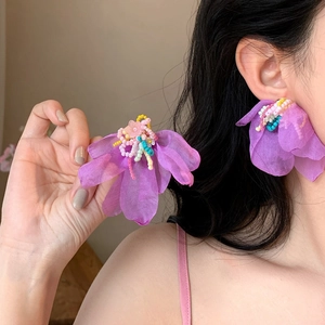 Primer plano de pendientes de flores de gasa morada con cuentas de colores en modelo asiática.