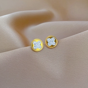 Golden clover stud earrings with crystal inlay and ribbed metal frame on silk background