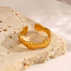 Polished gold bamboo joint stainless steel open ring displayed on a natural stone base