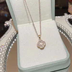 Gold clover necklace with zircon pendant on blue velvet jewelry box and pearls