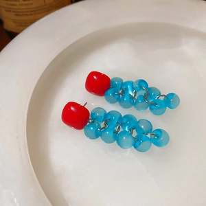 Detail view of square red resin studs with translucent blue grape tassel beads on white ceramic