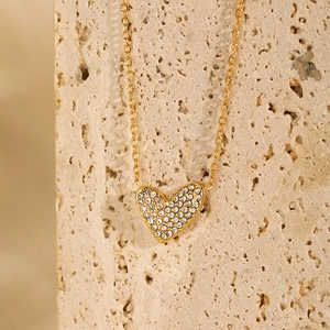 Detail of gold heart pendant with micro-set zircons on a textured stone surface