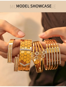 Close-up of four layered gold-plated bracelets featuring honeycomb and tree of life designs