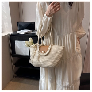 Detail of woven straw tote bag with leather flap, pearl buckle and lace bow accent