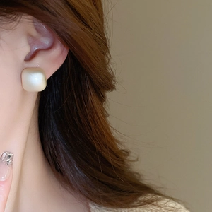 Close-up of a matte geometric square pearl earring on model with elegant nail art details
