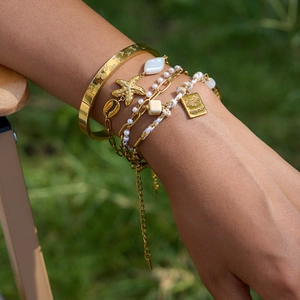 Détail du bracelet multicouche doré avec breloques étoile de mer perles et passeport
