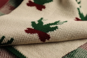 Close-up of knit fabric showing festive holly patterns in red and green on beige base