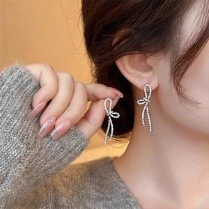 Detailed view of silver bow drop earrings with micro-pave crystals on model