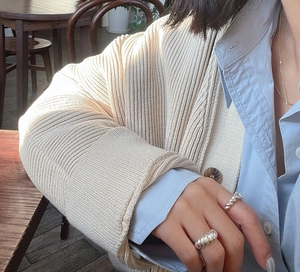 Close-up of 925 sterling silver croissant rings styled with a beige knit cardigan