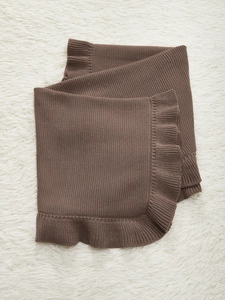 Detailed knit texture and ruffle edge of dark brown cotton baby blanket on plush rug