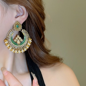 Detail of ethnic gold drop earrings with green enamel and pearl fringe on model