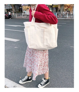 Grand sac cabas en toile blanche avec poches frontales porté sur l'épaule par un mannequin