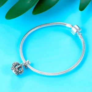 Detail of silver snake chain bracelet with oxidized crown pendant on blue background