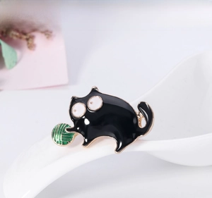 Detail of a black cartoon cat enamel brooch playing with a green ball of yarn