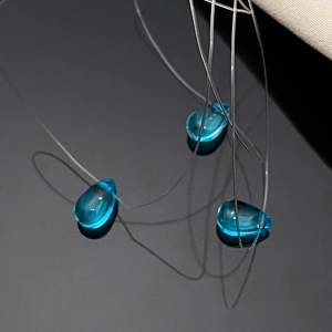 Detailed view of three blue teardrop pendants on a clear invisible fishing line cord