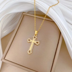 Close-up of golden hollow cross pendant with clear crystals on beige box with silk