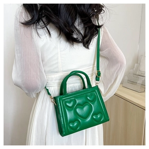 Sac bandoulière vert à motif cœur en relief porté sur une robe blanche élégante