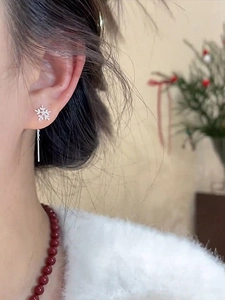 Macro shot of silver snowflake earrings with hanging chain on ear in a festive setting