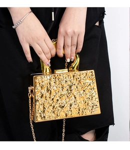 Detalle de bolso de fiesta dorado con textura martillada y asa superior escultural
