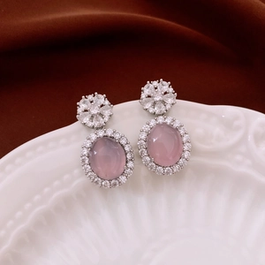 Detailed close-up of pink oval chalcedony earrings with floral zircon accents on white porcelain