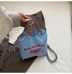 Detail of light blue nylon bag featuring red floral embroidery and checkered drawstring