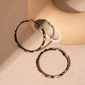 Close-up of vintage leopard print leather hoop earrings on a beige textured stone background