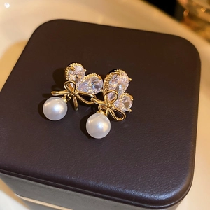 Detail of gold bow earrings with sparkling cubic zirconia and elegant white pearls