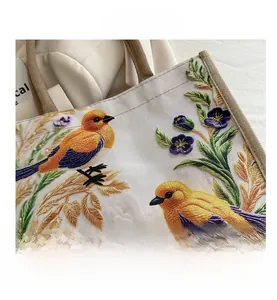 Close-up of intricate bird and floral embroidery on textured canvas tote bag fabric