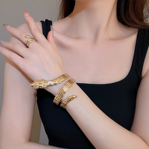 Detail of gold snake-shaped bangle and ring set with intricate scale textures on a wrist