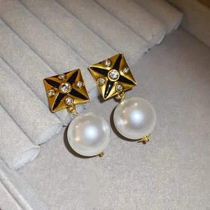 Detail of square gold stud earring with black enamel star and dangling white pearl