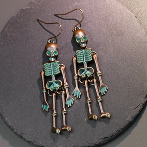Detailed view of articulated skeleton earrings with antique brass finish on dark slate