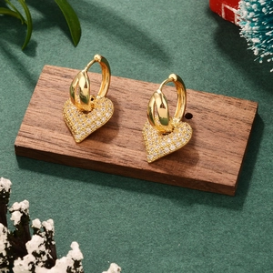 Elegant gold heart stud earrings with clear crystals on a dark wood and green backdrop