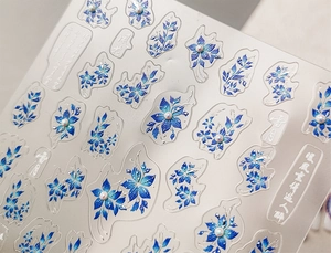 Macro view of blue floral nail stickers with white pearl accents and Chinese calligraphy