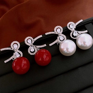 Macro view of bow-knot pearl drop earrings in red and white on black leather display