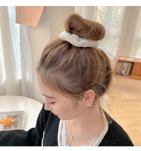 White fluffy scrunchie made of pleated fabric styled on a messy bun hairstyle