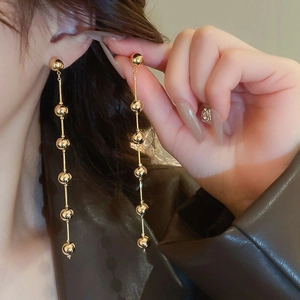 Detail of long gold drop earrings with polished beads on a female model for a luxury look